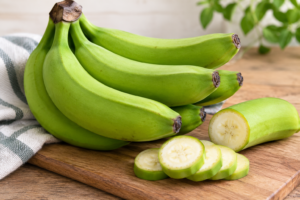 Fresh green bananas with slices on a wooden cutting board